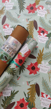A roll of personalized wrapping paper with Christmas-themed designs including trees, berries, and snowflakes, placed next to a label that reads 'Merry Christmas'.