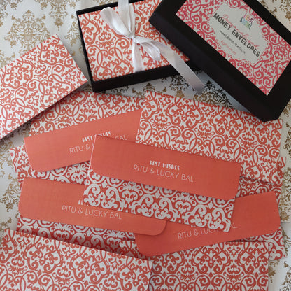 A flat-lay of money envelope gift set, featuring patterned envelopes, a black gift box with a white ribbon, and an open black envelope on a patterned fabric background.