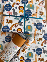 a gift wrapped in personalised wrapping paper with cute jungle animals design of a lion, monkey, elephant, giraffe , a cannister and a rolled sheet of paper