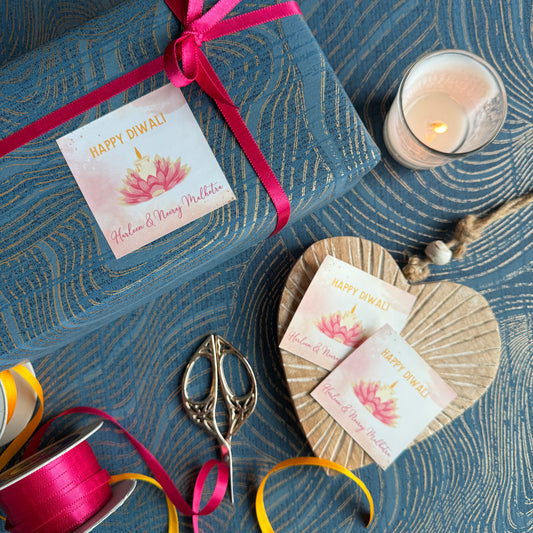 Gift box with 'Happy Diwali' card, ribbons, and a candle on a decorative surface.