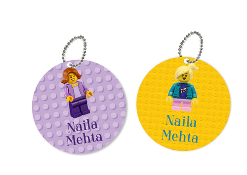 Two round metal bag tags with Lego character depictions, one featuring a purple character with a paisley pattern, and the other featuring a yellow character with a plain background.