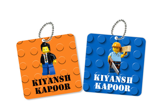 Two square metal bag tags with a lego character and the names KYANSH KAPOOR and KYANSH KUMAR on them, one orange and one blue with a chain attached.