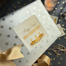 Gift box with a personalized card on a decorative surface with candles and ribbons.