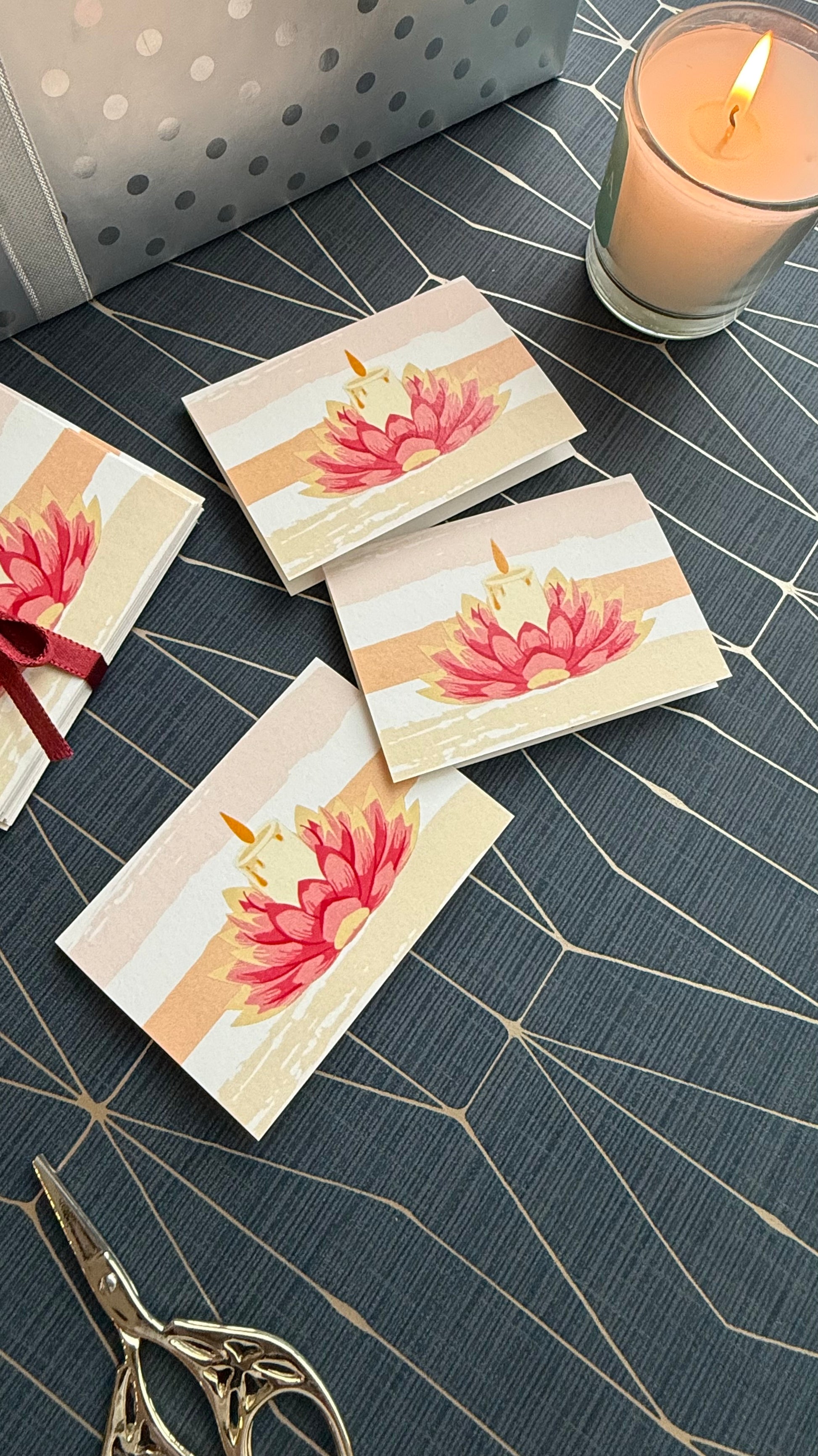 Set of greeting cards with floral design on a textured surface with a candle and scissors.