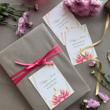 Gift wrapped in gray paper with pink ribbon, accompanied by floral cards and candles on a textured surface.