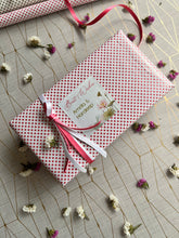 Gift wrapped in ink and white polka dot paper with a decorative lotus flower deisng gift label on a textured surface with small flowers.