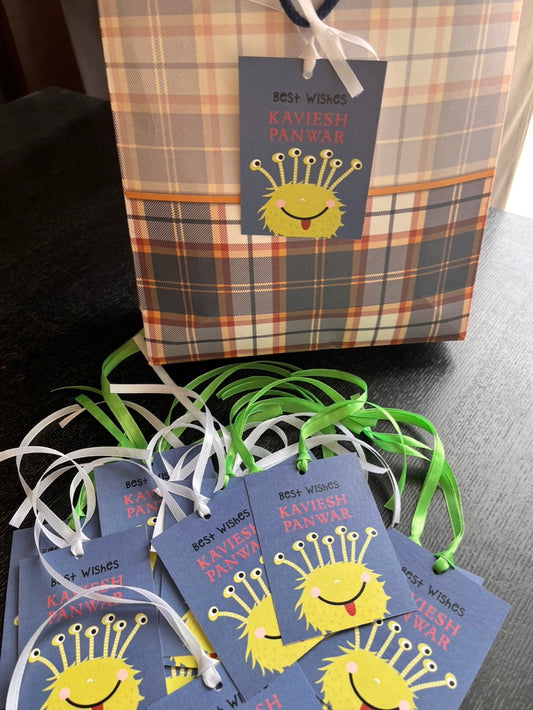 A plaid gift bag and several matching gift tags tied with green and white ribbons, printed with a yellow cartoon monster face and the text 'BEST WISHES KAVIESH PANWAR'.