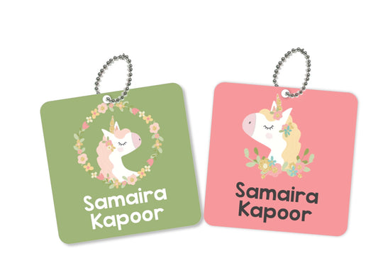 Two Square metal bag tags with unicorn and floral designs, one pink and one green, with the names printed on them.