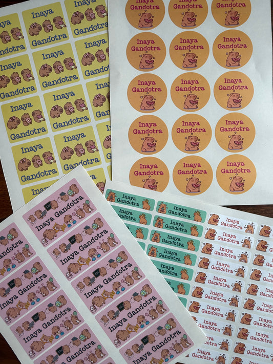 waterproof personalised school name labels printed sticker sheets laid out on a dark surface, featuring capybara illutrations