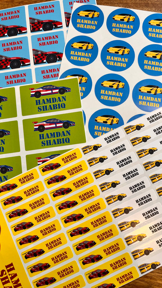 Custom car-themed sticker sheets featuring the names 'HAMBAN SHABIQ' in red text, alongside sports car illustrations and blue circular stickers, arranged on a wooden surface.