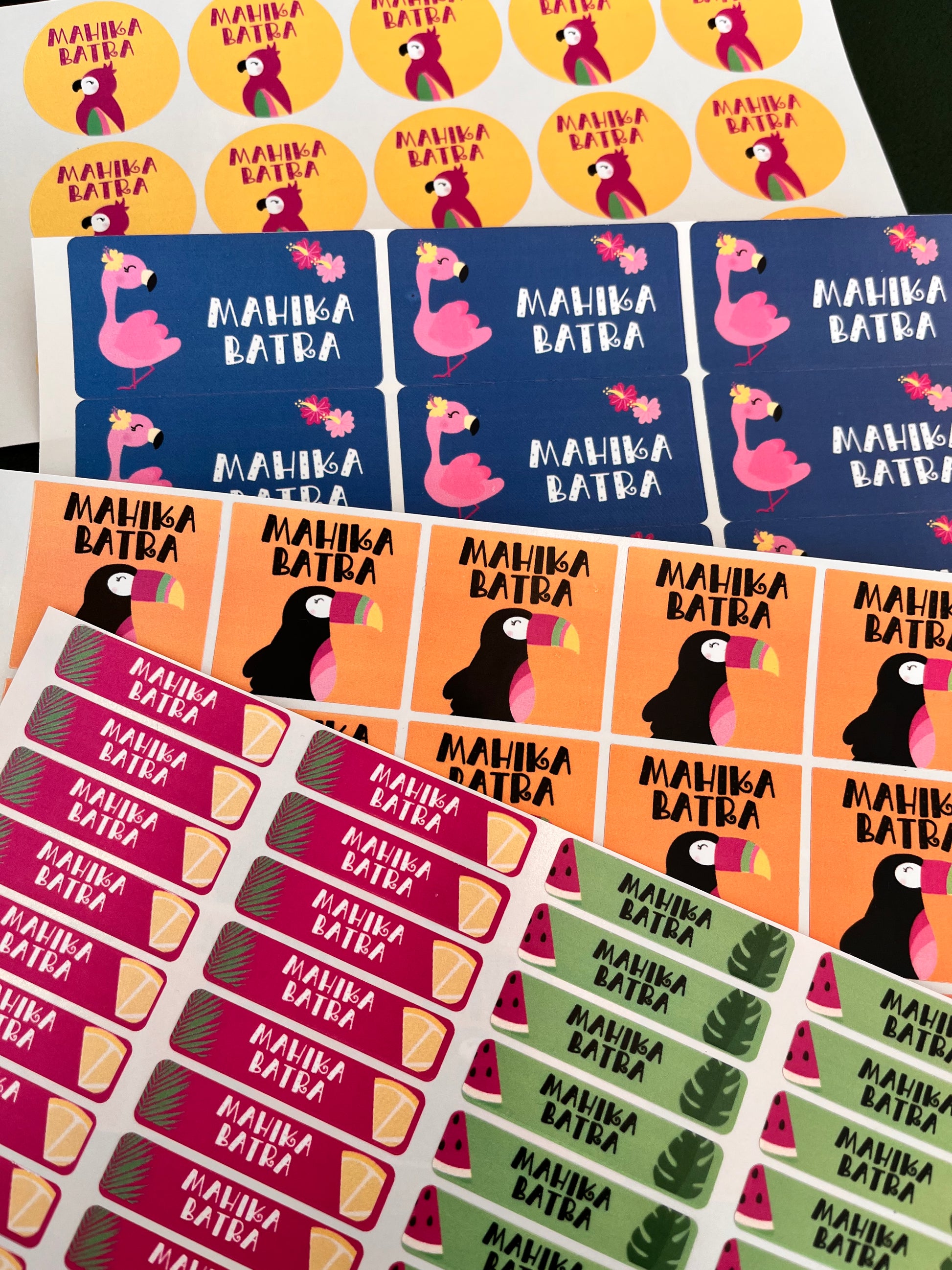 waterproof name labels with yellow ,  blue orange back grounds with illustrations of with black toucan i ice cream cones, green leaves, palm leaves.