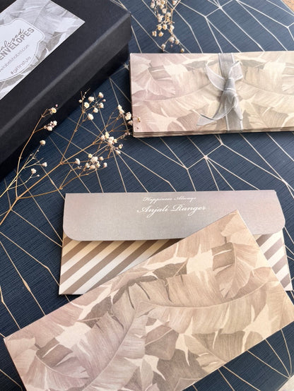 A styled flat-lay of elegant stationery, featuring a gift envelope with a beige and gray tropical leaf pattern