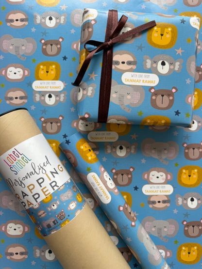 A roll of wrapping paper and a wrapped gift box with a matching pattern. The wrapping paper has a light blue background decorated with cartoon animals in yellow, brown, and gray, along with small white labels.