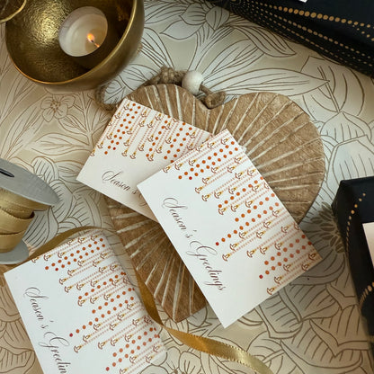Set of cards with 'Season's Greetings' text on a decorative surface with candles and ribbons.