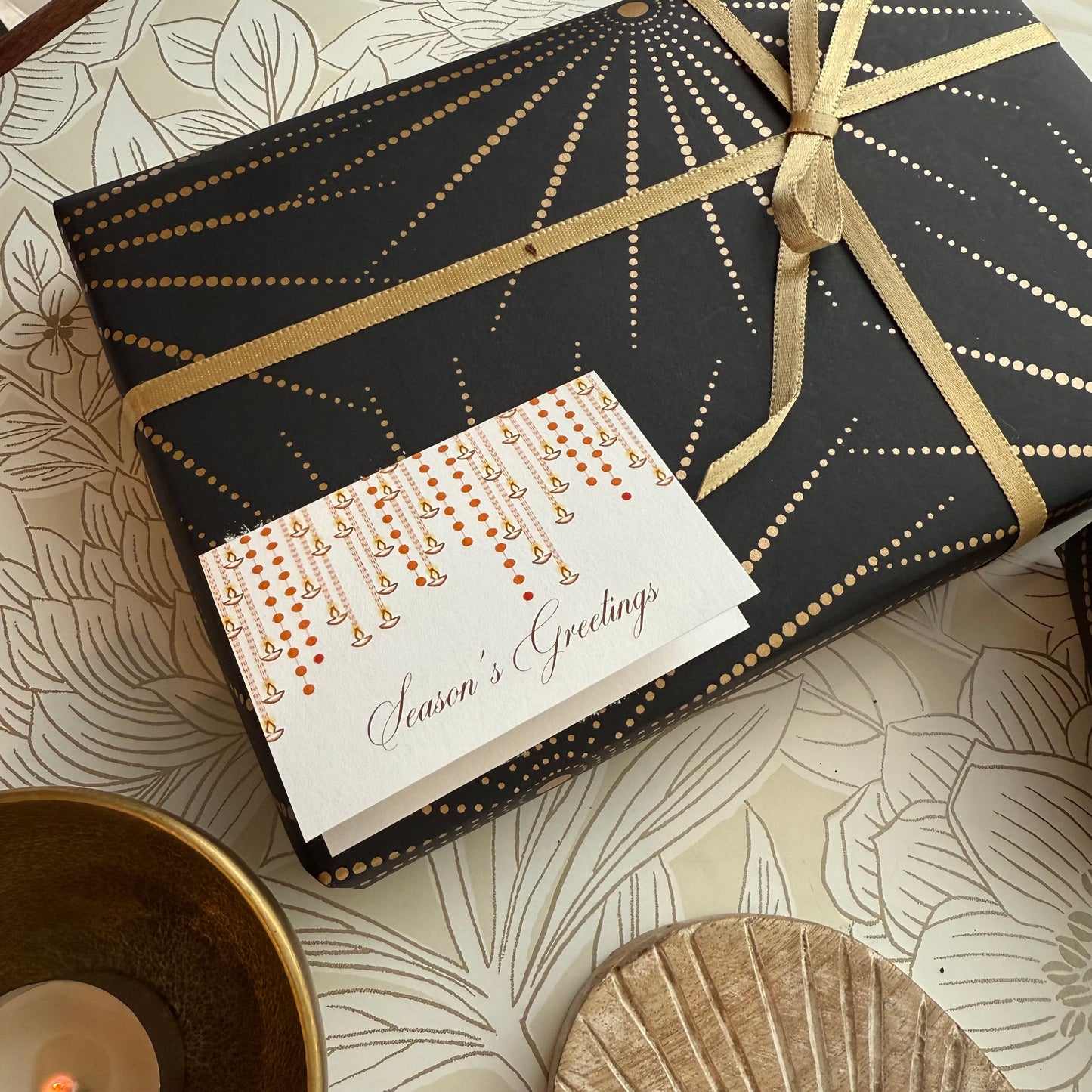 Gift box with gold ribbon and 'Season's Greetings' card on a decorative surface