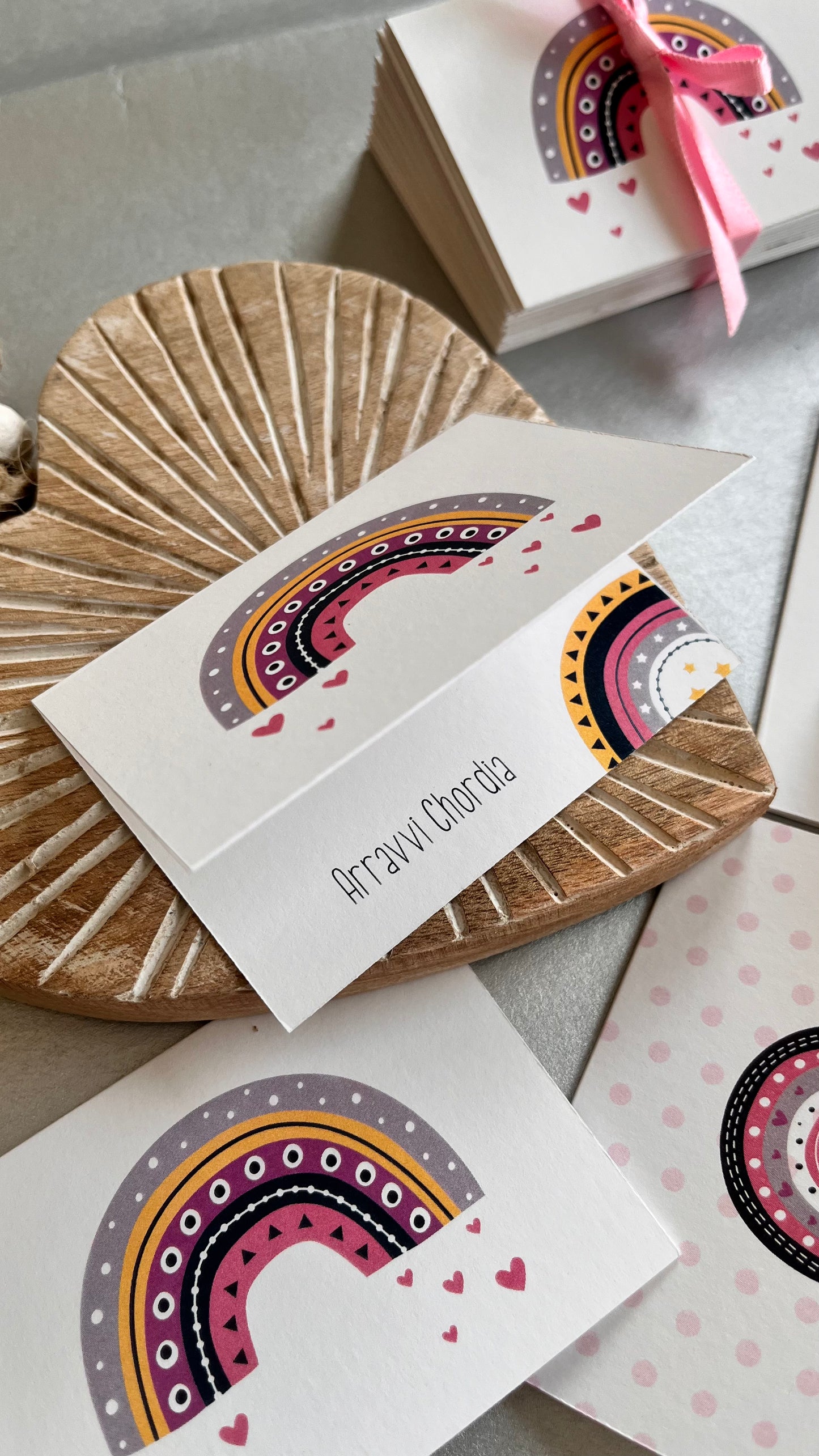 Folded gift tag personalised with a name featuring a colourful cute rainbow and hearts on a wooden heart on a white background 