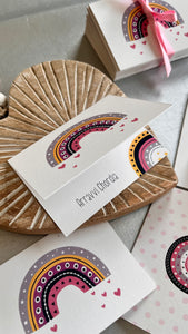 Folded gift tag personalised with a name featuring a colourful cute rainbow and hearts on a wooden heart on a white background 