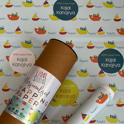Personalized wrapping paper set featuring a brown kraft cardboard tube and rolled sheets printed with a colorful sailboat pattern, tied with an orange ribbon, on a matching patterned background. Visible text includes 'Kajal Kanojiya' and 'Love From Kajal Kanojiya'.