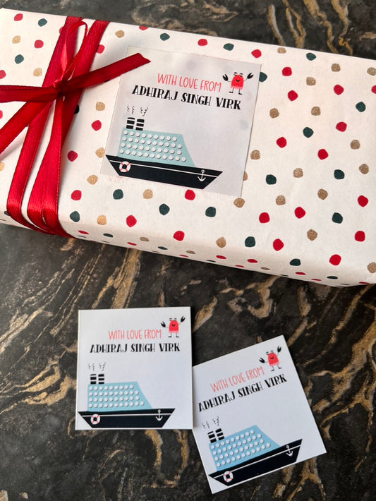 A wrapped gift box and two matching gift tags on a dark marble surface. The wrapping paper is cream with red, green, and beige polka dots and tied with a red ribbon.