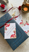 Gift wrapped in blue paper with a floral card, scissors, and a candle on a textured surface.