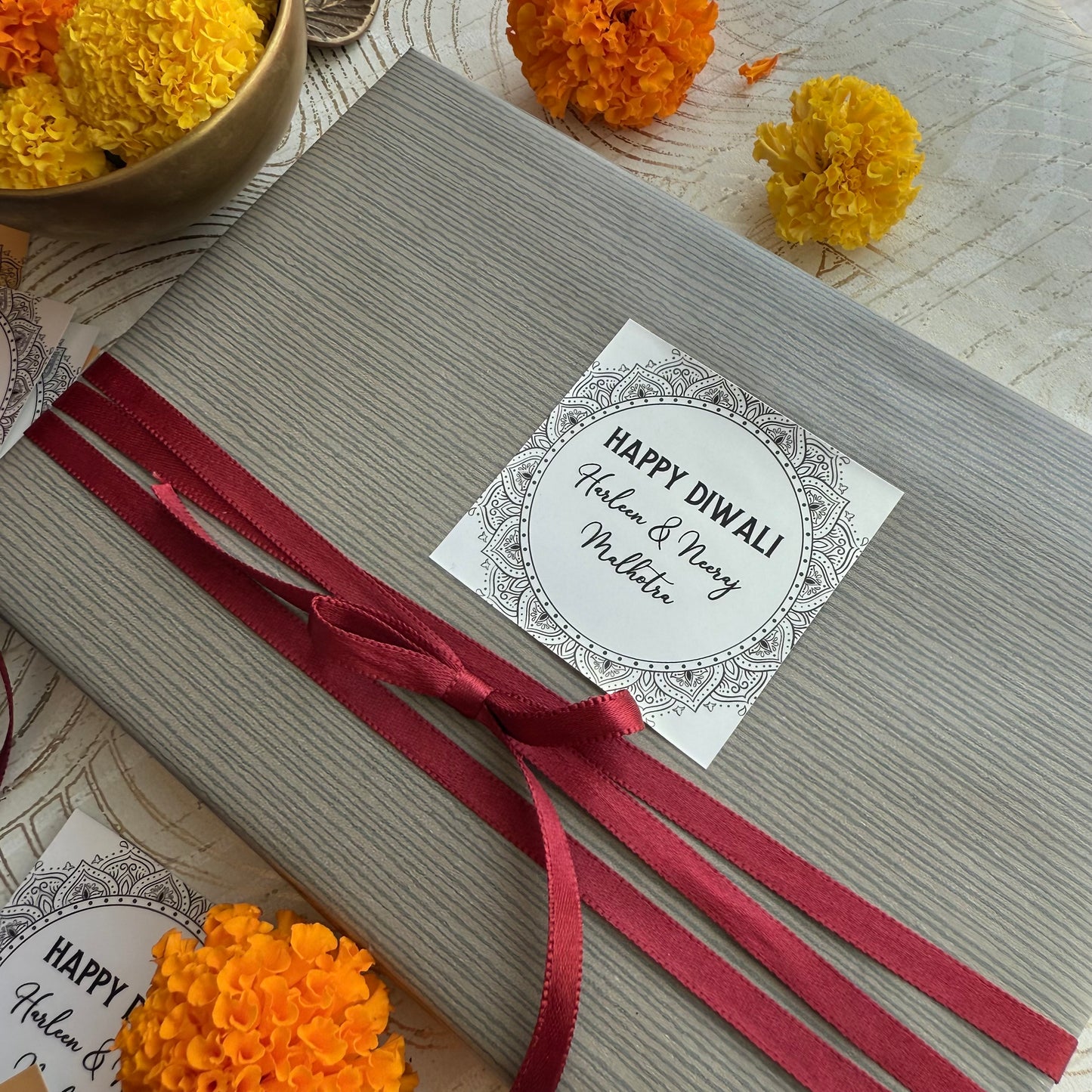 Gift box with a red ribbon and 'Happy Diwali' card, surrounded by decorative marigold flowers.