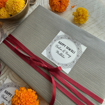 Gift box with a red ribbon and 'Happy Diwali' card, surrounded by decorative marigold flowers.