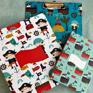 A set of school supplies with a pirate-themed design, including a notebook, a clipboard, and a folder, each featuring colorful illustrations of pirates, ships, and sea creatures.