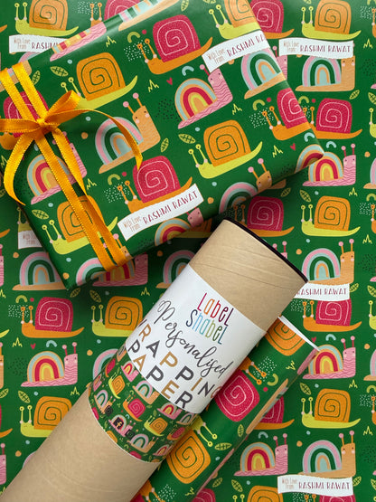 A roll of wrapping paper and a wrapped gift box with a matching patterned wrap, featuring a colorful retro snail design on a green background. The gift is tied with a yellow ribbon, 
