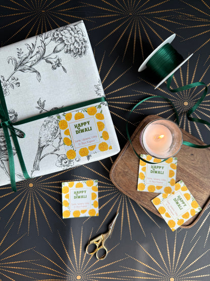 Diwali gift labels with yellow marigold design  on a gift wrapped box a candle on a decorative background.