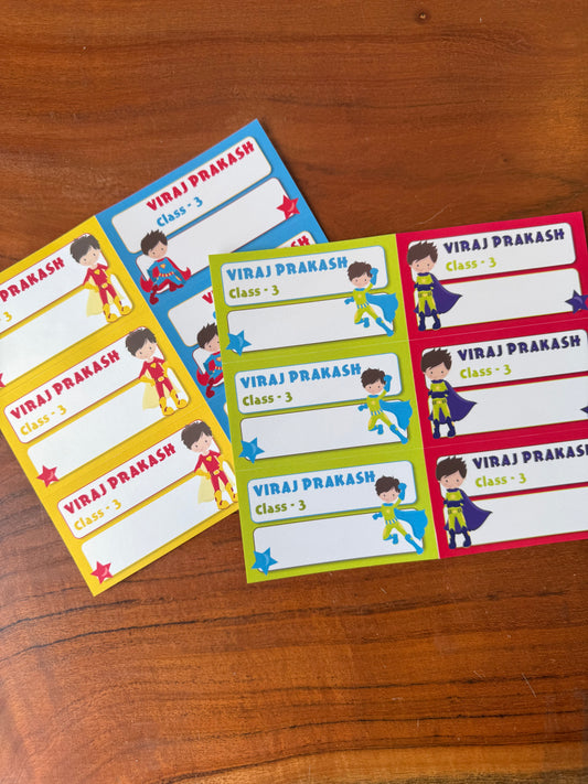 4 colorful superhero-themed book labels  feature different border colors (yellow, blue, green, and red) with a consistent design including a cartoon running superhero, the name 'VIRAJ PRAKASH', and 'Class - 3'.