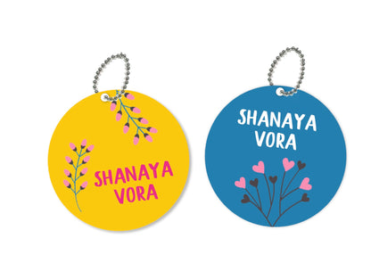 a pair or round metal bag tags with blue and yellow backgrounds and some flowers int he front with a name