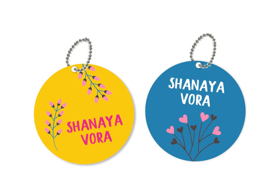 a pair or round metal bag tags with blue and yellow backgrounds and some flowers int he front with a name