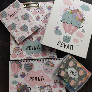 a set of 5 items clipboard notebook folder art book and box of personalised crayons with a pastel colours of airbaloons and flowers clouds moon