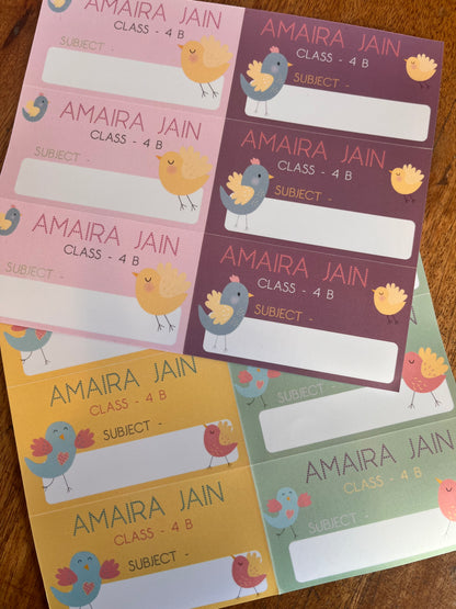 colorful book labels with cartoon bird illustrations, arranged in a fan shape on a wooden surface. The labels feature different pastel colors (purple, pink, green, yellow) 