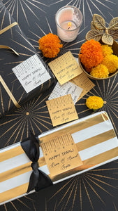 Decorative gift wrapping with gold ribbon, black bow, and marigold flowers on a black and gold patterned background.
