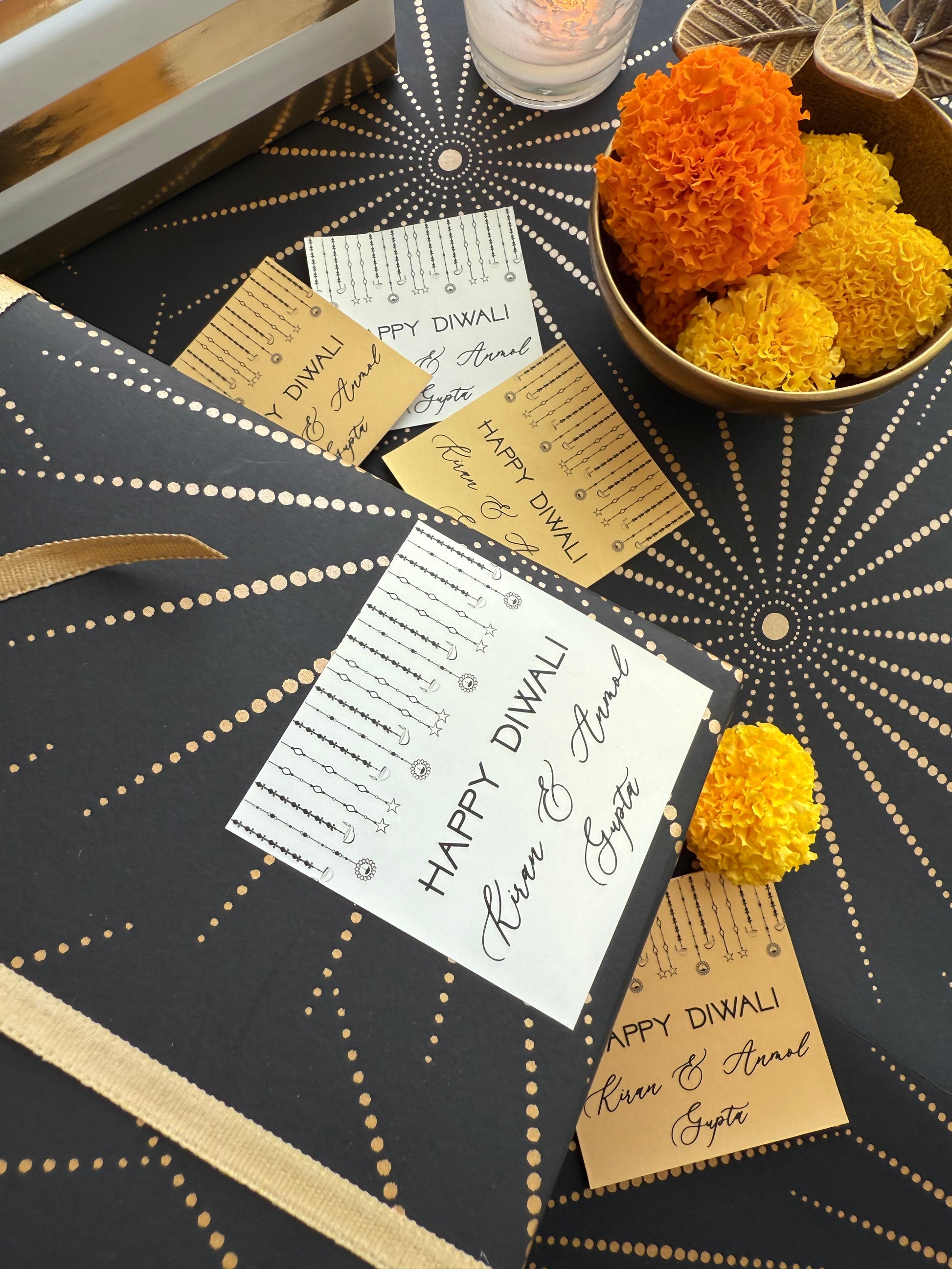 Decorative table setting with 'Happy Diwali' cards and marigold flowers on a black and gold patterned tablecloth.