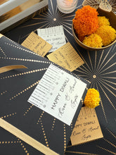 Decorative table setting with 'Happy Diwali' cards and marigold flowers on a black and gold patterned tablecloth.