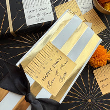 Gift box with gold and black design, 'Happy Diwali' tag, and decorative elements on a patterned background.
