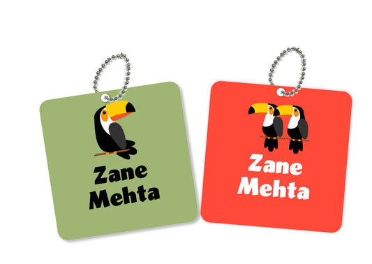 Two round metal bag tags with a toucan design, one green and one red, both with the name 'Zane Mehta' printed on them.