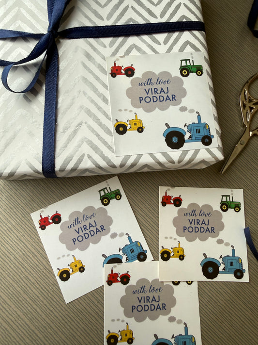 A wrapped gift box and several printed labels with colourful tractors as a design.  The gift wrap is white with a light gray geometric pattern and tied with a dark blue ribbon.