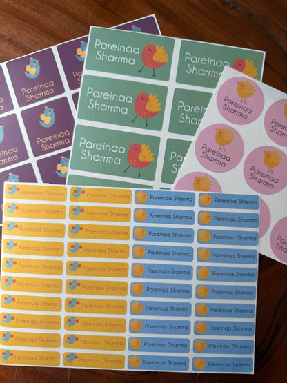 Several printed sticker sheets laid out on a wooden surface, featuring the text 'Pareinaa Sharma' with small cartoon bird illustrations. The sheets include purple, green, yellow, and blue color schemes.