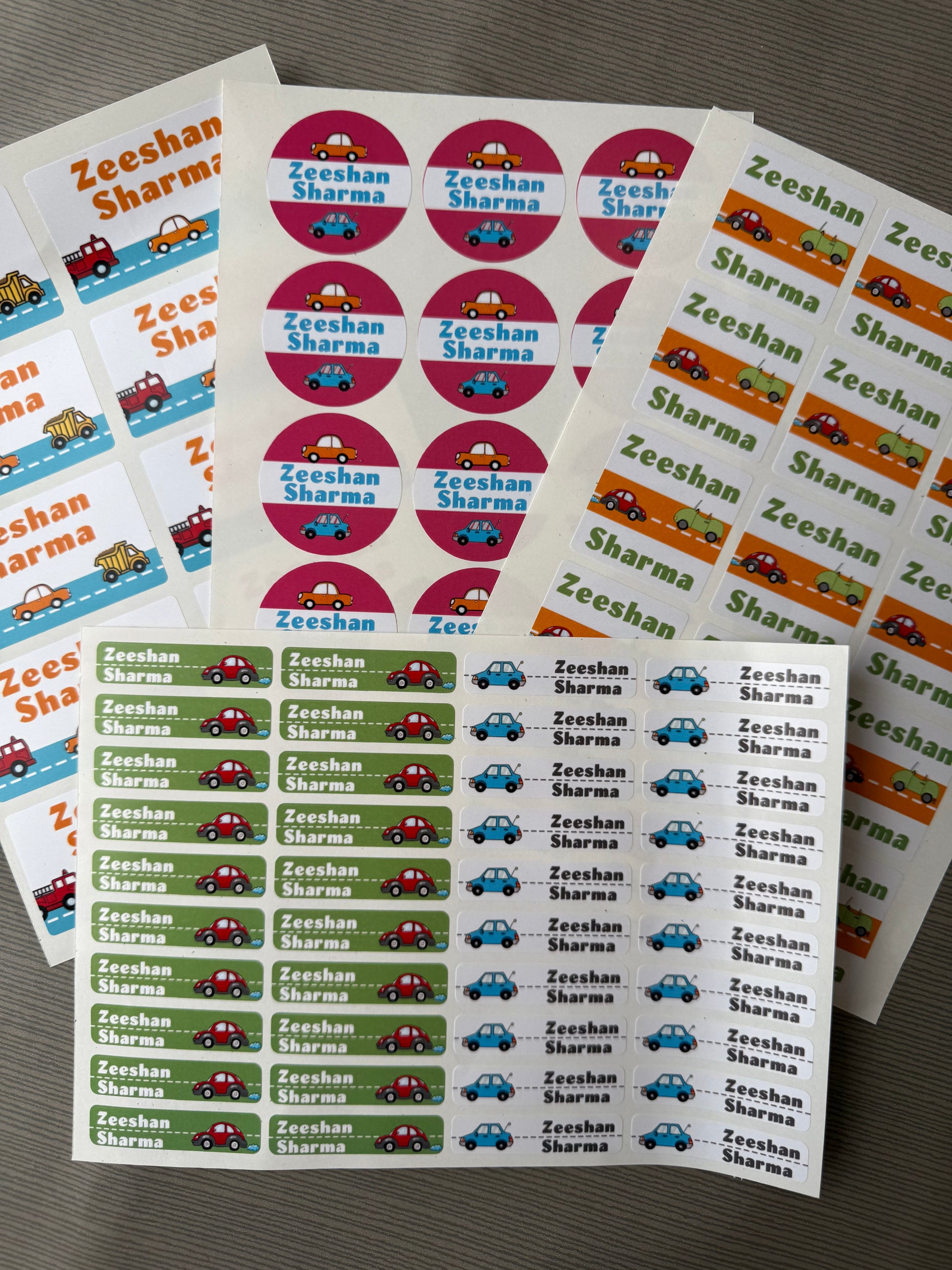 Customizable waterproof school  name stickers featuring the name 'Zeeshan Sharma' with small car illustrations, shown in multiple sheets with pink, green, blue, and orange accents.
