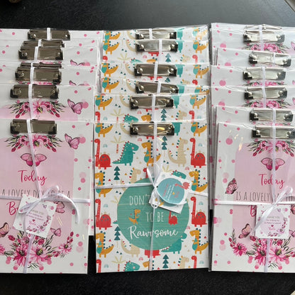 Packages of clipboards with attached cards, featuring various designs such as floral and geometric, tied with white ribbons.