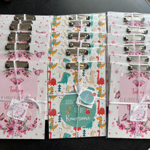 Packages of clipboards with attached cards, featuring various designs such as floral and geometric, tied with white ribbons.