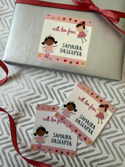 A silver gift box wrapped with a red ribbon and three matching personalized gift tags laid on a gray-and-white chevron fabric. The tags feature a cartoon girl and the text 'with love from SAMAIRA DASGOPTIA'.