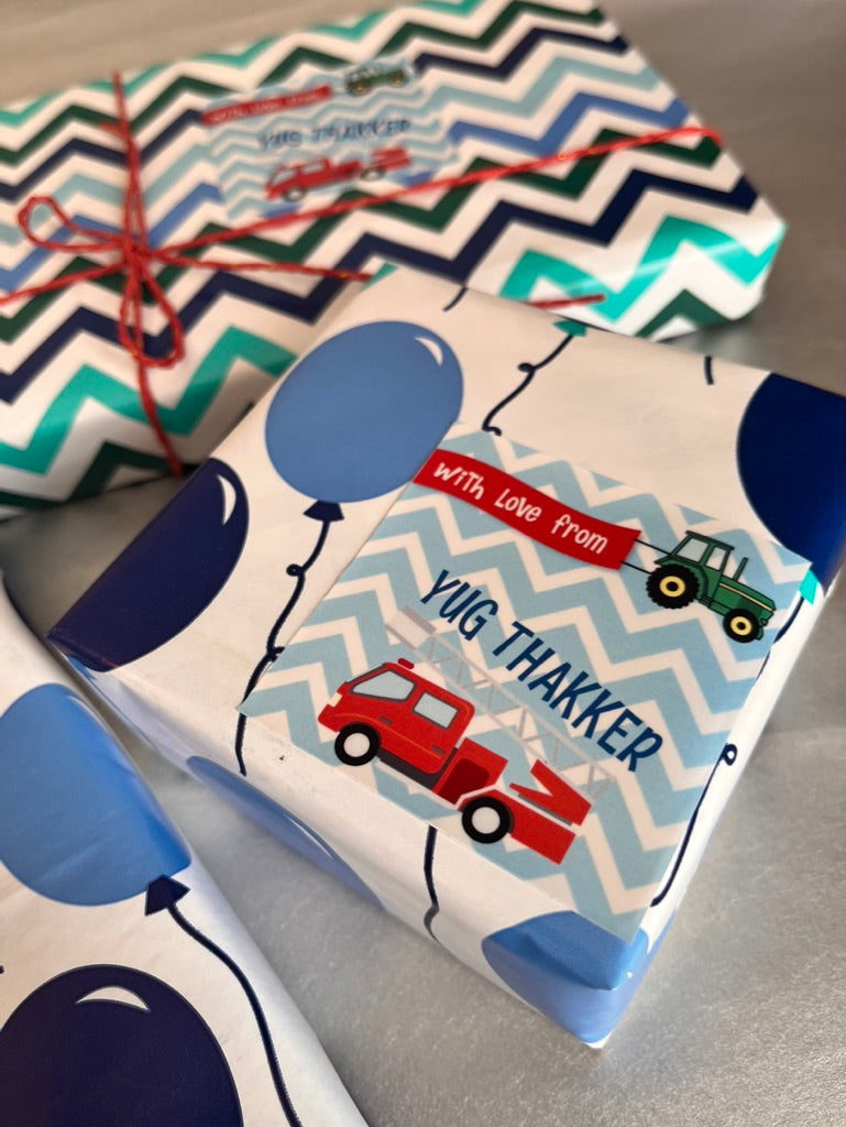Personalized baby shower gift wrap featuring a blue and white chevron pattern with balloon and tractor illustrations, tied with red string.