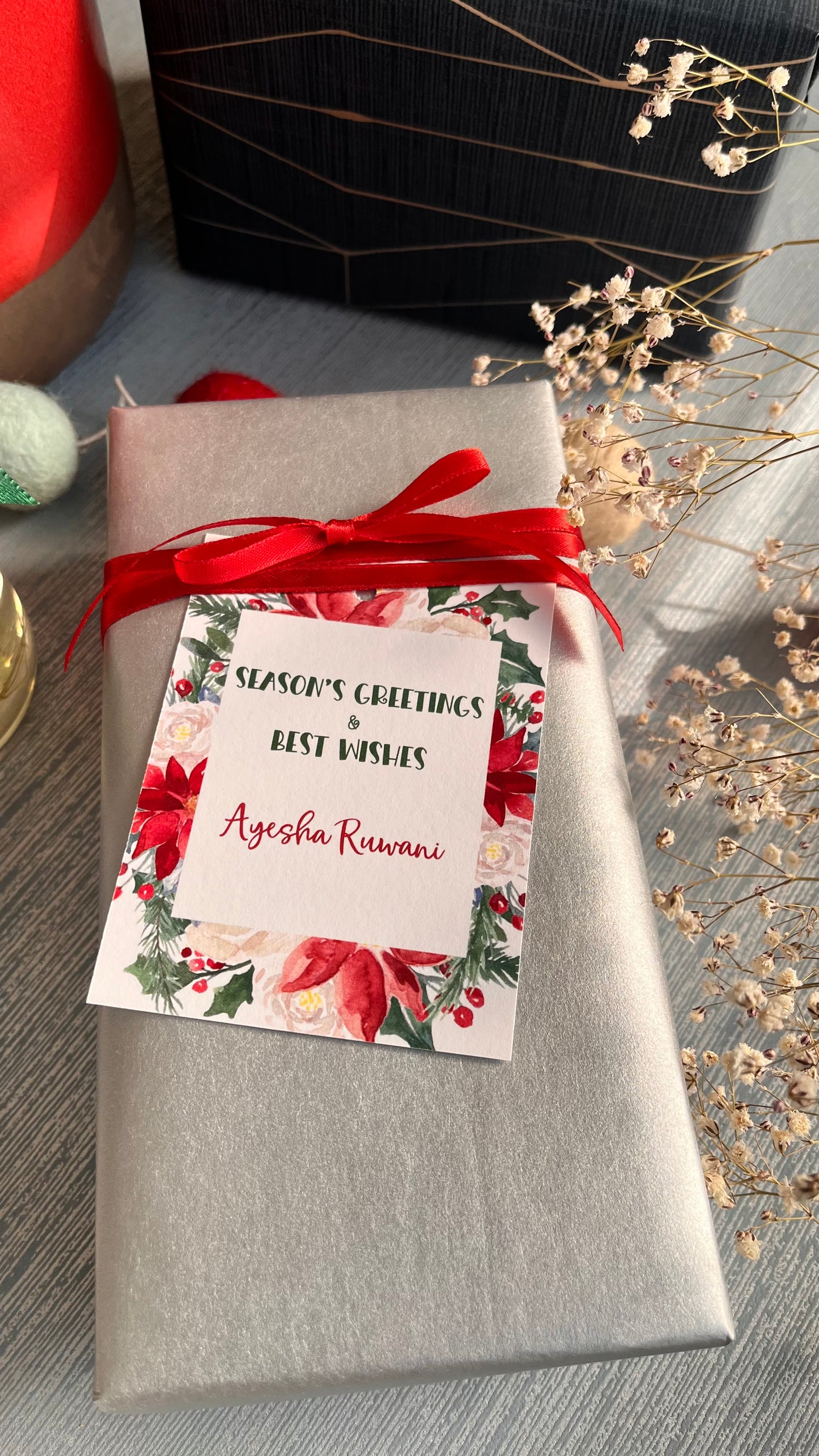 Xmas ribbon tag with bright xmas foilage in shades of green red tied with a red ribbon on a silver paper wrapped gift