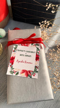 Xmas ribbon tag with bright xmas foilage in shades of green red tied with a red ribbon on a silver paper wrapped gift