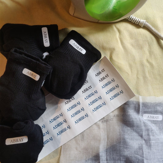 Black socks with iron on name  label on a white paper with text, on a yellow surface.