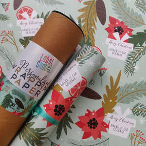 A roll of personalized wrapping paper with Christmas-themed designs including trees, berries, and snowflakes, placed next to a label that reads 'Merry Christmas'.